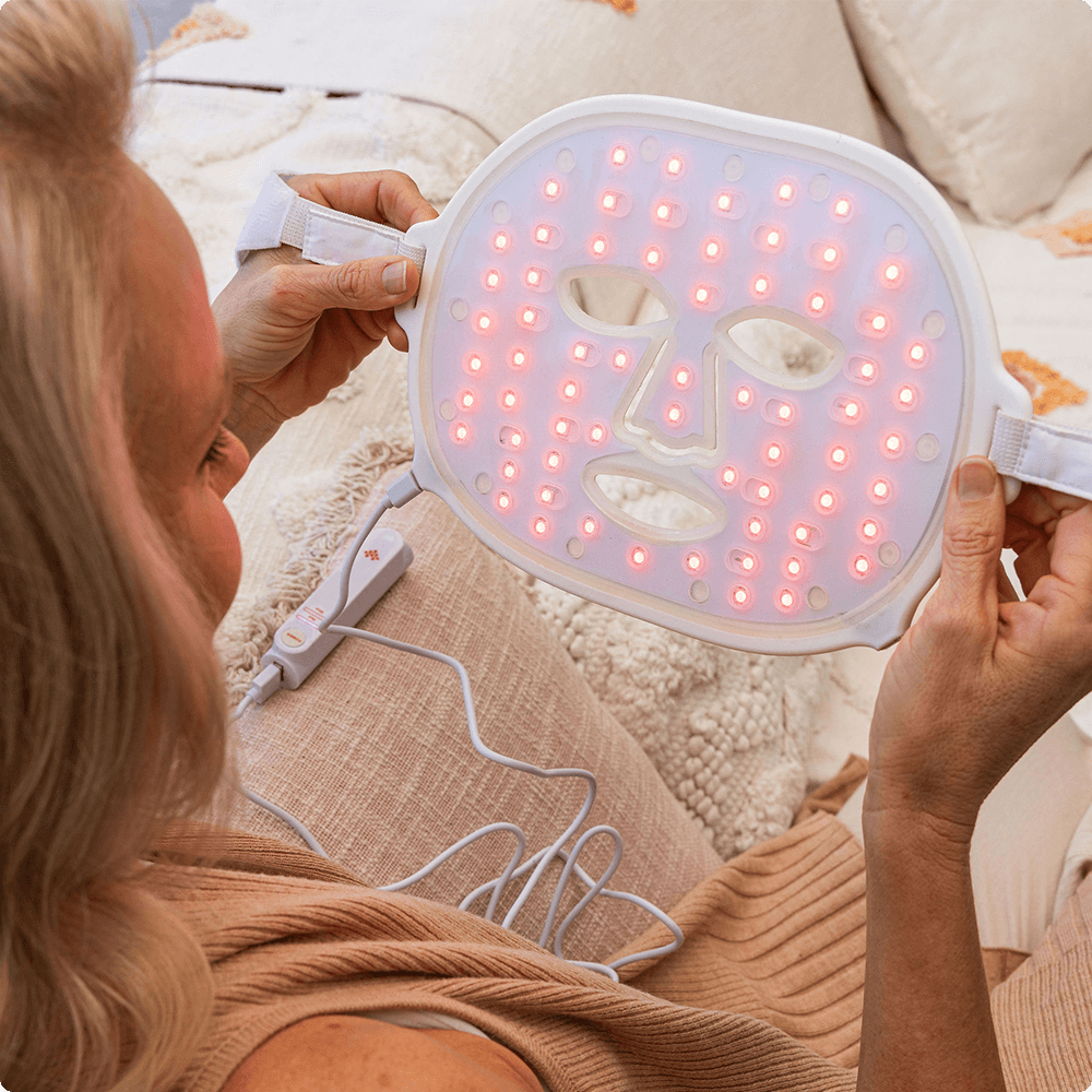 Woman holding Infraredi LED Red Light Therapy Mask for skincare at home.