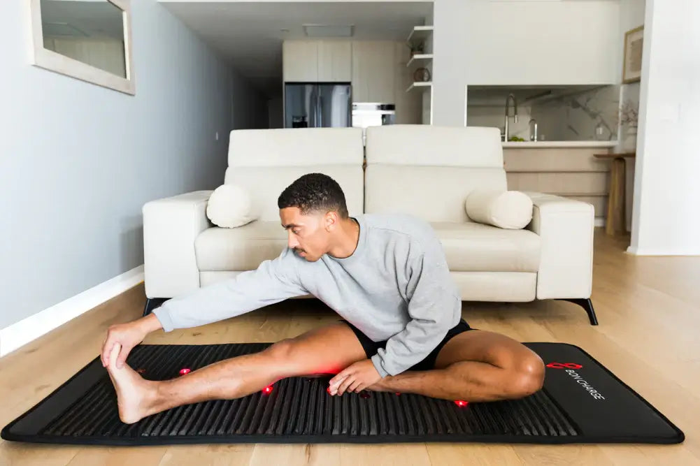 Person stretching on Bon Charge Infrared PEMF Mat Max in living room, enhancing recovery and wellness with pemf mat therapy.