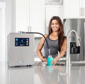 Woman using Echo Ultimate Hydrogen Water Machine in kitchen for enriched water.