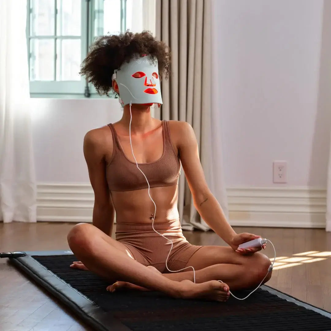 Woman using Kala Red Light Therapy Mask for skincare routine indoors.