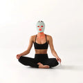 Woman wearing Kala red light therapy mask sitting in meditation pose, showcasing LED red light therapy for facial rejuvenation.