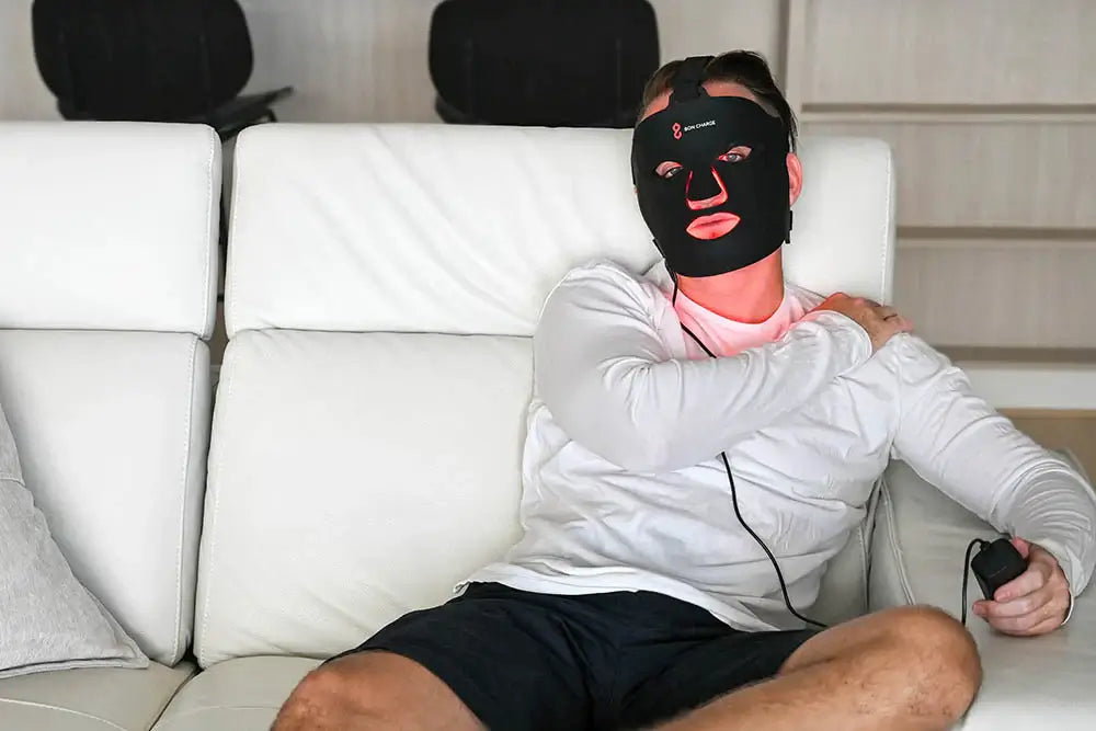 Person using Bon Charge Red Light Face Mask for skincare therapy on a couch.